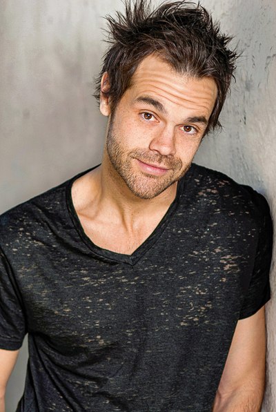 Person in a black T-shirt with a relaxed expression against a light wall.