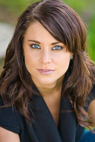 Close-up of a person with dark hair and a black jacket against soft greenery.