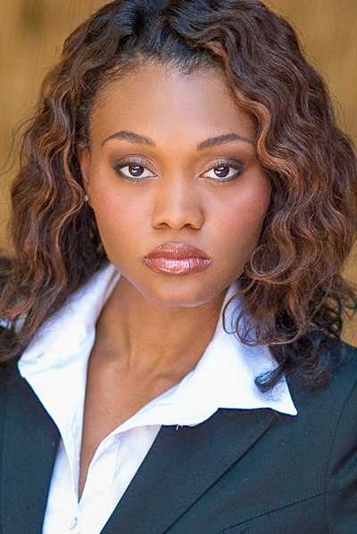 Person with curly hair in a dark blazer and white collared shirt.