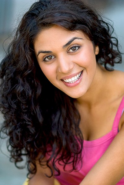 Smiling person with dark curly hair wearing a bright pink top.