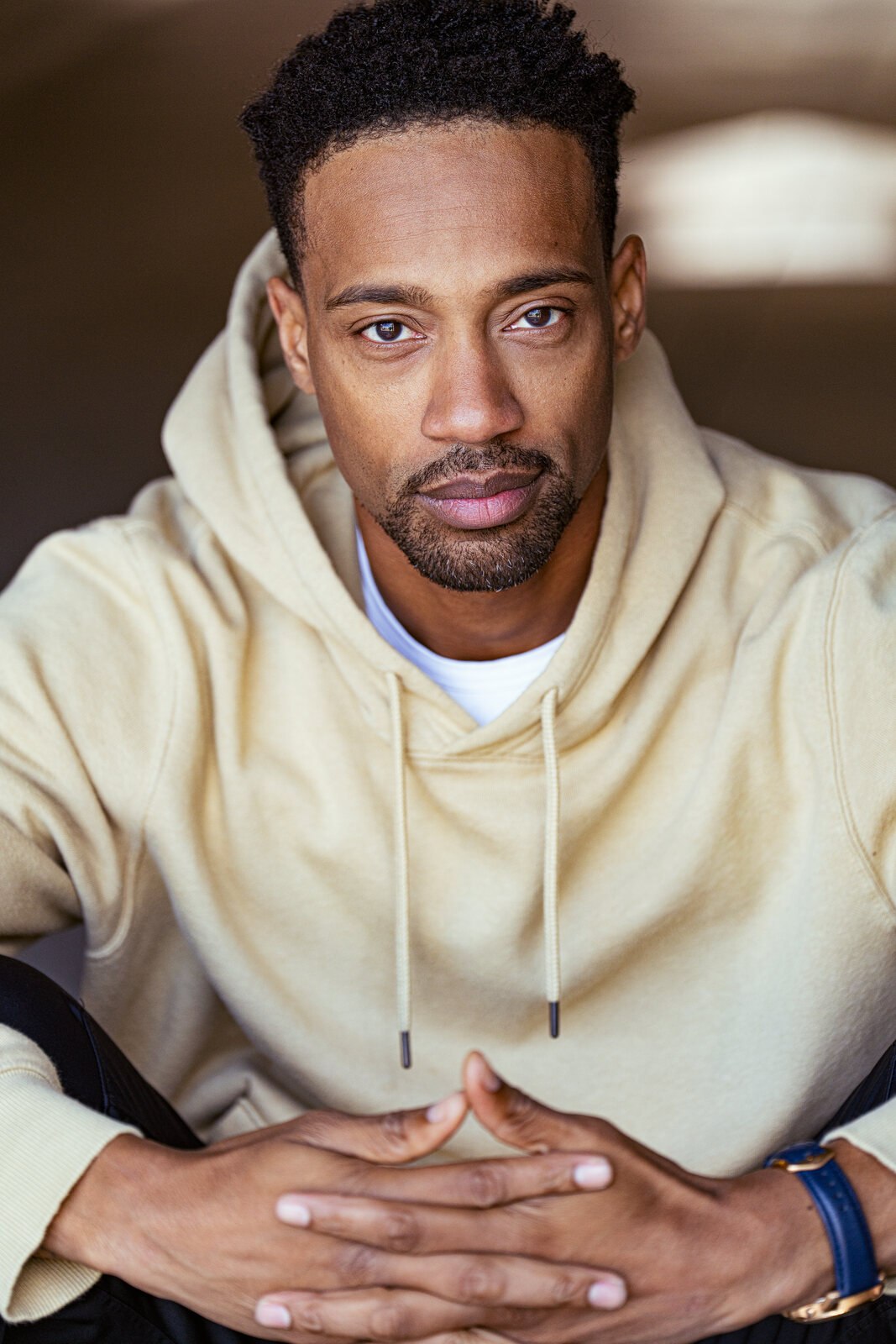 Seated person in a cream shirt with hands loosely joined, looking at the camera.