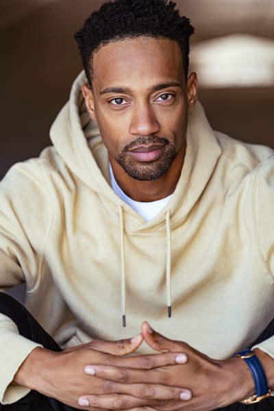 Seated person in a cream shirt with hands loosely joined, looking at the camera.